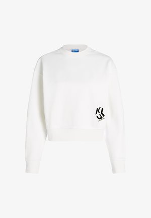Bela dolgodlaka majica s črnim stiliziranim logotipom "KL" in majhnim besedilom na spodnjem desnem sprednjem delu.