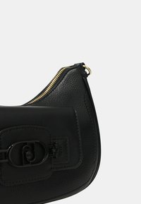 Borsa a mano in pelle nera con una forma curva, dotata di chiusura con zip e una prominente fibbia frontale. Finitura texture. Dettagli in hardware dorato.
