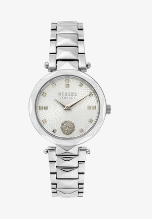 Reloj plateado con una caja octogonal, esfera blanca texturizada, marcadores cuadrados de horas y un emblema de león. Pulsera de eslabones de metal con un acabado pulido.