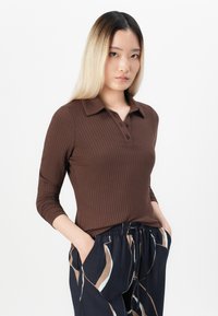 Polo marron à manches longues en maille côtelée avec un col, présentant une patte de boutonnage. Assorti à un pantalon à motifs, ample et doté de poches.