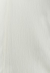Gros plan d'un tissu blanc texturé avec des lignes verticales ondulées et droites créant un motif à rayures subtil.