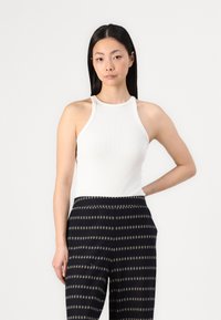 Λευκό ριμπ αμάνικο τοπ με στρογγυλή λαιμόκοψη. Συνδυασμένο με παντελόνι wide-leg με σχέδια που διαθέτει οριζόντιες ρίγες σε σκούρους τόνους.