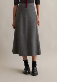 Fustă midi din lână gri, cu o textură netedă, formă evazată și talie înaltă, asortată cu mocasini negri și șosete negre cu model în relief.