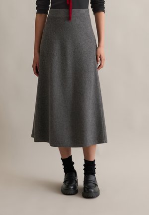 Grauer Woll-Midirock mit glatter Textur, ausgestellter Form und hohem Taillenbund, kombiniert mit schwarzen Slippern und gerippten schwarzen Socken.