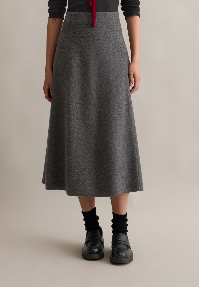 Fustă midi din lână gri, cu o textură netedă, formă evazată și talie înaltă, asortată cu mocasini negri și șosete negre cu model în relief.