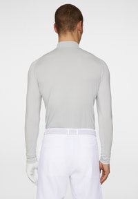 Camicia a maniche lunghe di colore grigio chiaro con colletto alto. I pantaloni bianchi presentano una cintura intrecciata. La texture è liscia, adatta per l'abbigliamento sportivo.