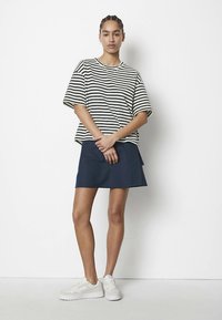 Kortærmet top med striber i creme og marineblå, kombineret med en mørkeblå nederdel. Outfitet afsluttes med hvide sneakers.