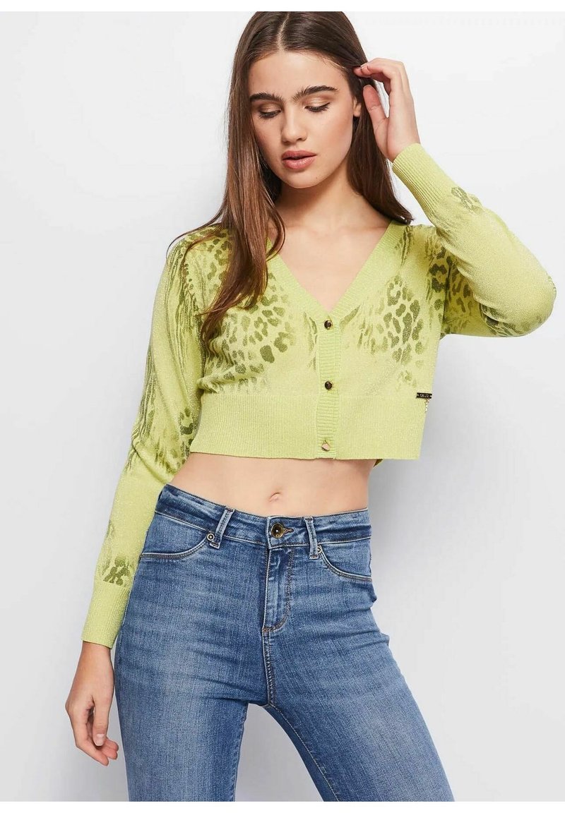 Limegroene cropped cardigan met een v-hals, lange mouwen en een luipaardpatroon. Bevat knoopsluiting en geribbelde textuur. Gekozen in combinatie met blauwe jeans.