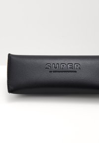 Kovový puzdro na okuliare z čiernej kože s embosovaným logom "SUPER". Hladký povrch, valcovitý tvar a zosilnené švy na okrajoch.