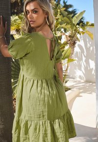 Grünes, gestuftes Kleid aus strukturiertem Stoff mit kurzen Puffärmeln und einer gebundenen Rückendetail. Das Design hat eine fließende Form und einen lässigen Stil.