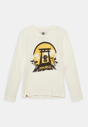 Weißes Langarmshirt mit schwarzem und gelbem Ninjago-Design, das eine Ninja-Figur unter einem Torii-Tor mit Bäumen und Wolken zeigt.