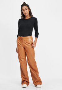 Zwart longsleeve top gecombineerd met tan leren wijde broek, met een ritssluiting aan de voorkant en een gladde textuur, aangevuld met witte sneakers.