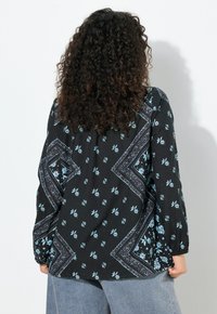 Blusa negra con estampado de flores azul claro. Presenta un ajuste relajado y mangas largas, con una tela texturizada y detalles únicos en los bordes.
