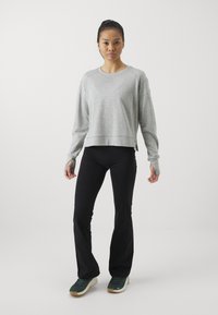 Lys grå, kort sweatshirt med rund halsringning og lange ærmer; kombinert med svart vide bukser og grønne joggesko.