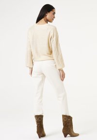 Beige gebreide trui met textuurmouwen, gecombineerd met witte slim-fit broek en bruine suède enkellaarzen met bloemendessin.
