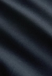 Gros plan sur un tissu sombre avec un motif de tissage diagonal subtil et des plis doux créant de légères variations d'ombre.