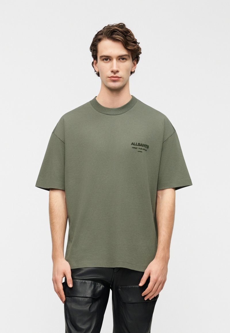 Λαδί oversized μπλούζα από βαμβάκι με κοντά μανίκια, που διαθέτει μικρό μαύρο λογότυπο στο αριστερό στήθος και στρογγυλή λαιμόκοψη.