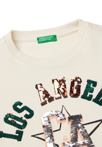 Sweat-shirt couleur crème avec un texte en sequins "LOS ANGELES CA" en vert, bronze et argent, accompagné d'un graphique d'étoile en dessous. Étiquette verte visible.