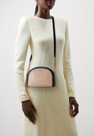 Compacte crossbodytas met een gebogen silhouet in roze en zwart leer, met een kettingriem en logodetail aan de voorkant.