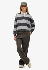 Gestreiftes graues und navyfarbiges, kurzes Poloshirt, kombiniert mit olivgrünen Jogginghosen mit Schriftzug. Als Accessoires sind eine passende Mütze und Sneakers enthalten.
