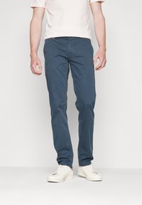 Herrblå chinos i bomull, slim fit med fickor, subtila sömdetaljer, tillsammans med vita sneakers. Slät textur.