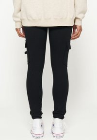 Zwarte cargoleggings van rekbare stof, met zijzakken en een tapered fit, gecombineerd met witte high-top sneakers.