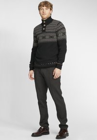 Suéter de punto negro con cuello alto, botones de madera y diseño estampado en tonos de gris y rojo. Combinado con pantalones gris y zapatos negros.