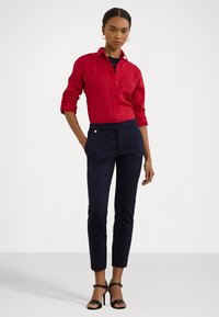 Red linen button-up shirt with rolled sleeves paired with navy tailored pants and black strappy heels, featuring subtle gold accents.