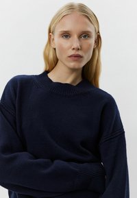 Mornarsko moder pulover iz pletene tkanine, z okroglo ovratnico in spuščeni rameni, z rebrastimi manšetami in robom za dodatne podrobnosti.