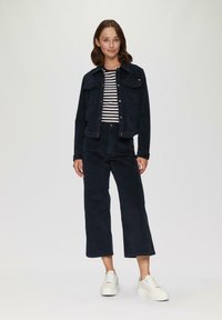 Granatowa kurtka z korduroyu z dwoma kieszeniami na piersi, zestawiona z granatowymi spodniami z korduroyu o wysokim stanie oraz białymi sneakersami na platformie. Pod spodem pasiasta koszula.