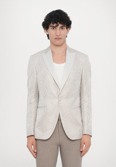 Light beige blazer with paisley pattern, satin shawl collar, single-button closure, paired with light brown tailored trousers.