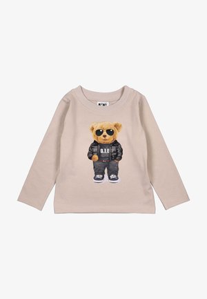 Beige lange mouwen shirt met een graphic van een beer in een zonnebril, zwarte jas, donkere broek en sneakers op de voorkant. Zachte stoftextuur.