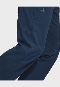 Navyblaue Hose aus glattem Material, mit einer seitlichen Tasche und dezentem Logodetail. Entworfen für Komfort und Bewegungsfreiheit.