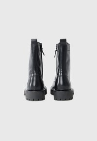 Bottines en cuir noir avec une finition lisse, dotées d'une fermeture éclair latérale, d'une semelle en caoutchouc résistante et d'une languette à l'arrière pour un enfilage facile.
