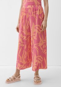 Roze en oranje wijde broek met een bladerenpatroon, gemaakt van een gestructureerde stof en voorzien van een elastische tailleband. G gedragen met lichtroze sandaaltjes met bandjes.