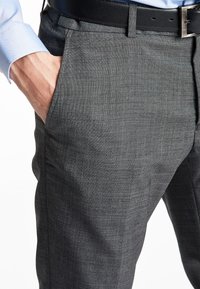 Pantaloni grigi a tessitura con finitura testurizzata, dotati di tasche laterali e una cintura nera. Una camicia azzurro chiaro è visibile dal polsino.