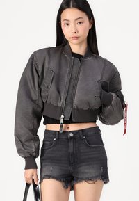 Cropped bomber jacket in dark gray fabric with ribbed cuffs and hem, featuring a frontal zipper and patch pockets. Paired with frayed black denim shorts.