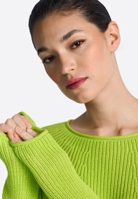 Jasnozielony sweter na drutach z teksturowanym wzorem i prążkowanymi mankietami, z szerokim dekoltem i podwiniętymi krawędziami dla swobodnego wyglądu.