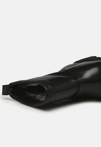 Stivale in pelle nera con una superficie liscia, punta arrotondata e una morbida fodera in pelliccia visibile all'apertura. Dotato di un pratico tallone laterale per un facile indosso.
