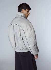 Giacca bomber imbottita grigia con colletto alto e piping nero lungo le cuciture. Polsini e orlo a coste, con vestibilità rilassata e tessuto morbido.