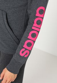 Grijze sweatshirt met lange mouwen, voorzien van een opvallend roze logo langs de arm. Gladde textuur, met een zak aan de voorkant.