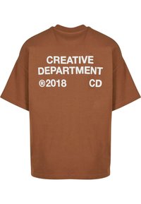 Brun bomulds oversized T-shirt med hvid tekst på ryggen: "CREATIVE DEPARTMENT ® 2018 CD." Korte ærmer, rund halshul.
