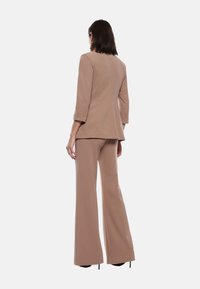 Completo due pezzi beige con giacca aderente a maniche tre quarti e pantaloni a gamba larga. Tessuto liscio e linee pulite.