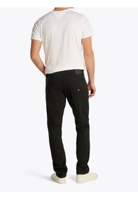 Valkoinen lyhythihainen paita, mustat kapeat housut ja vaaleat kengät. Housuissa on takatasku ja teksturoitu kangas; paidassa on yksinkertainen malli.