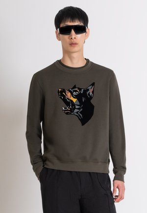 Sweat-shirt vert olive avec un motif de tête de chien en noir et orange, doté d'un col côtelé et d'une coupe décontractée.