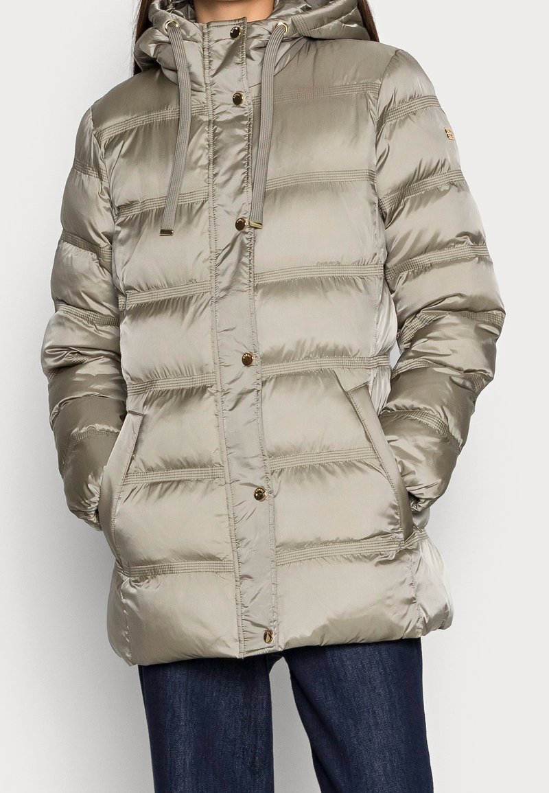 Giacca a vento in taupe chiaro, con cappuccio, bottoni frontali e pannelli imbottiti orizzontali. Texture liscia con finitura lucida.
