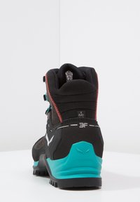 Black and teal hiking boot with a high ankle design, textured black upper, red accents, adjustable laces, and a rugged sole for traction.