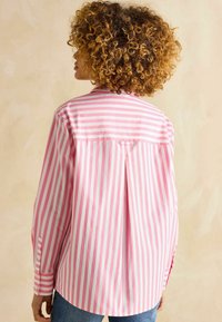 Rosa-weiße gestreifte Bluse mit einem Rückenfalten, Knopfmanschetten und einem Kragen; Baumwollstoff mit einer glatten Textur.