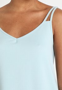 Ljust blå ärmlös topp med v-hals och tunna axelband. Slät textur med en enkel design utan synliga mönster eller utsmyckningar.