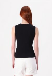 Svart ärmlös topp av mjukt tyg, figurnära design, med rund halsringning, i kombination med vita uppvikta shorts. Enkel och ren estetik.